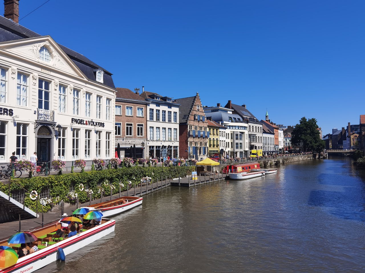 Charming canal in Gent, Belgium with vibrant architecture and moored boats on a sunny day.