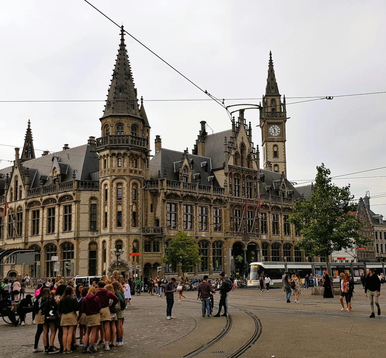 A bustling day at Korenmarkt in Gent, Belgium showcasing the historic clock tower and tram lines.